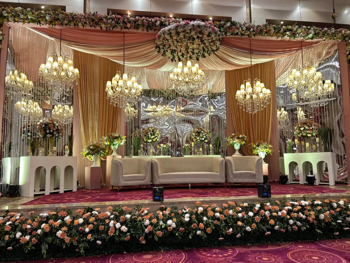 Peach drapes, crystal chandeliers and flowers framing a cream reception sofa