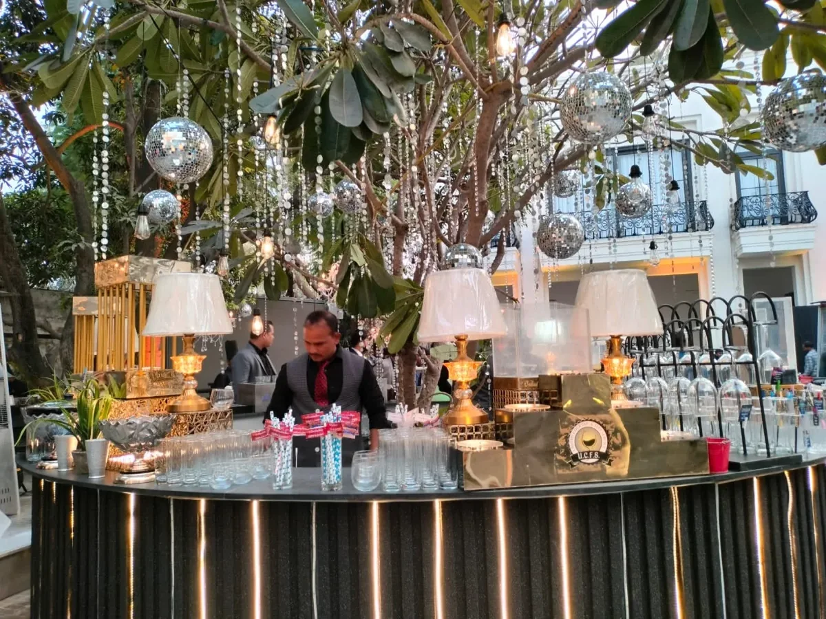 Outdoor bar with gold lamps and mirror balls suspended from a leafy tree