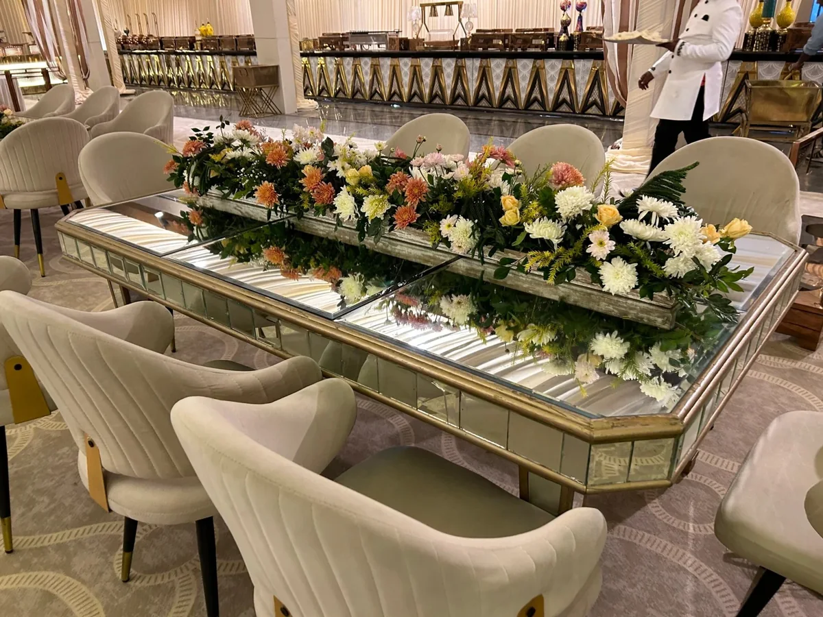 Mirrored dining table with a long pastel floral arrangement and ivory chairs