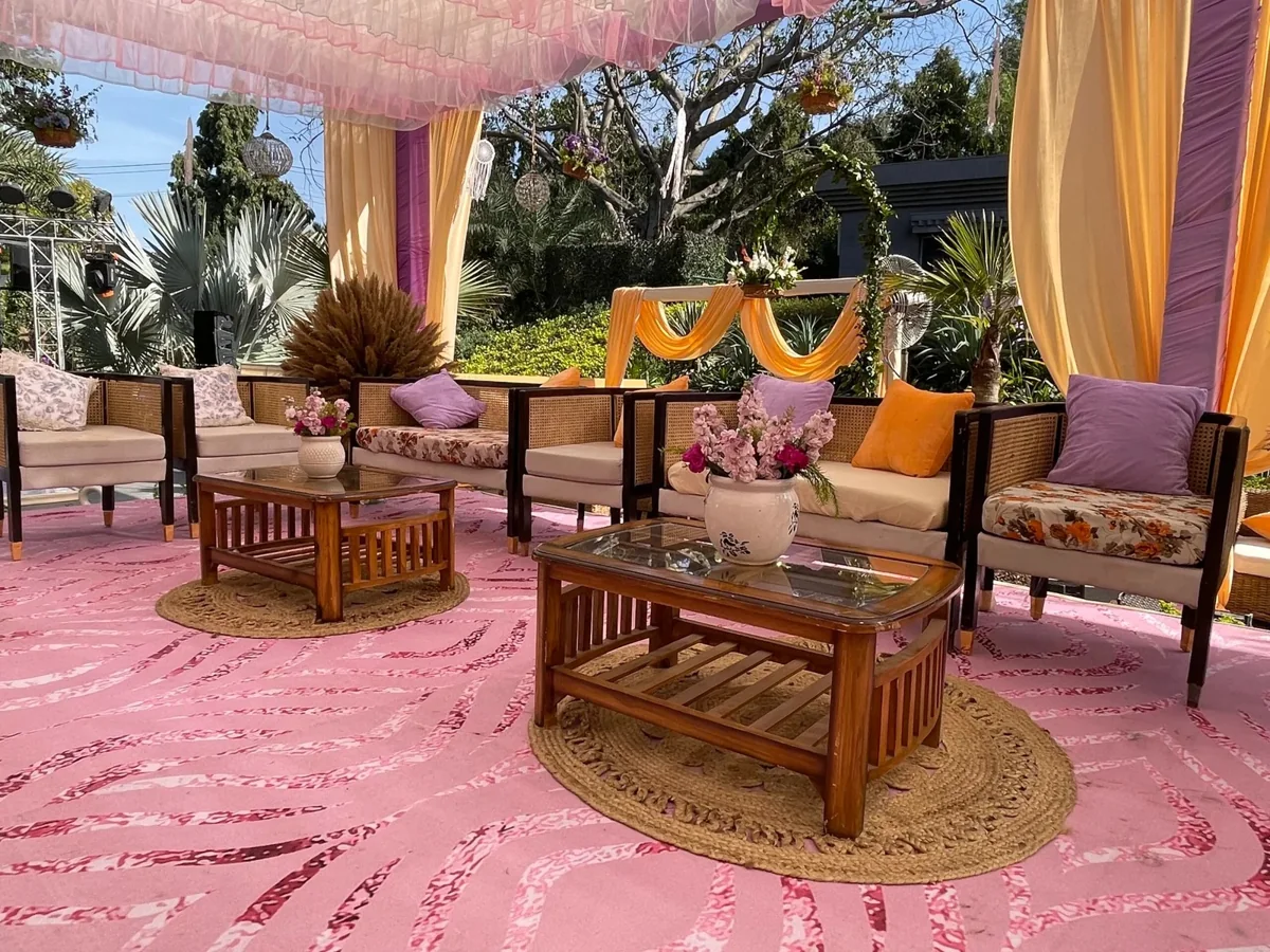 Rattan seating with lavender and orange cushions beneath pastel garden drapes