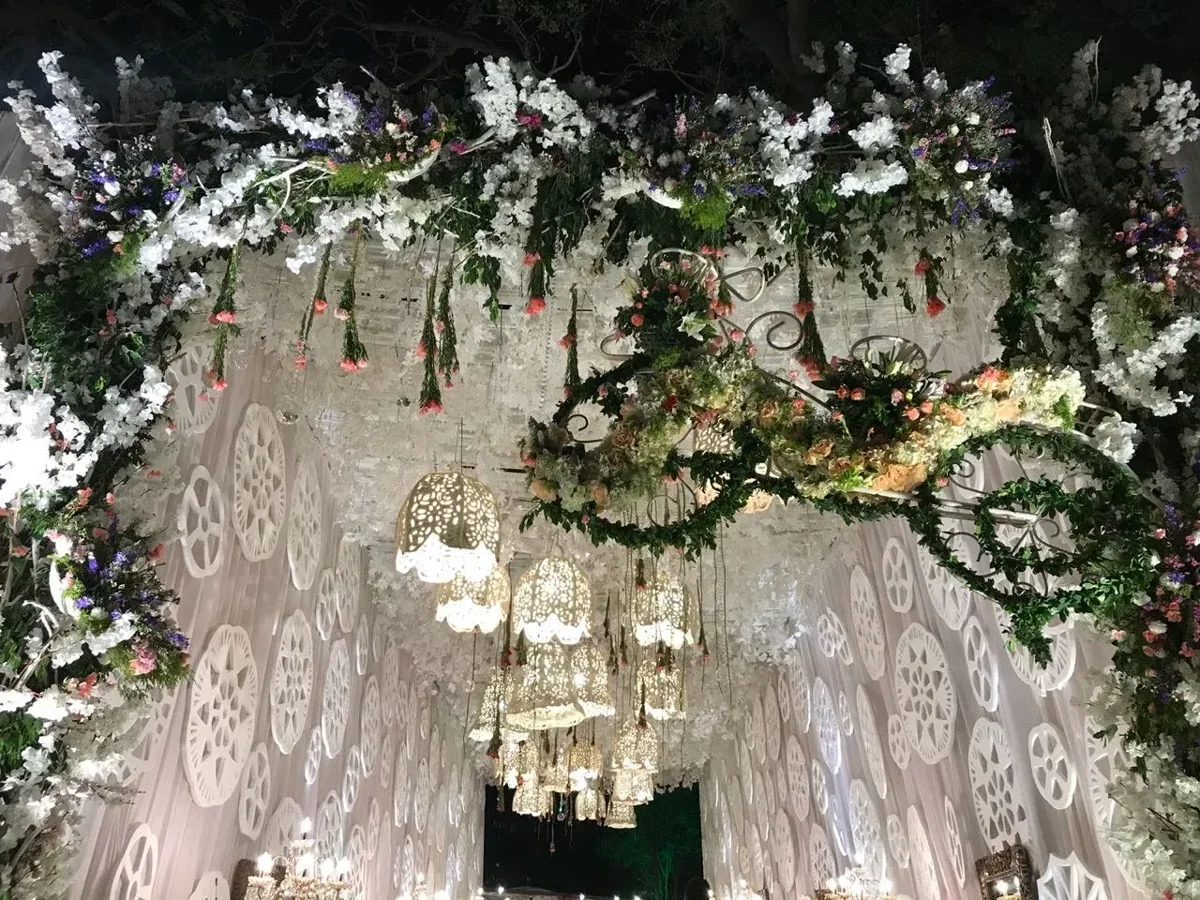 White lattice entrance with hanging lanterns, greenery and white flowers